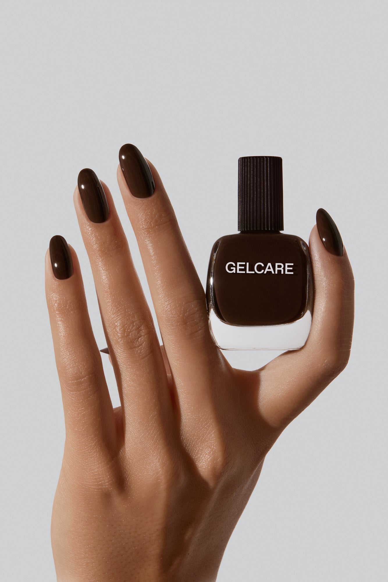 Bouteille de vernis brun café noir Gelcare dans une main