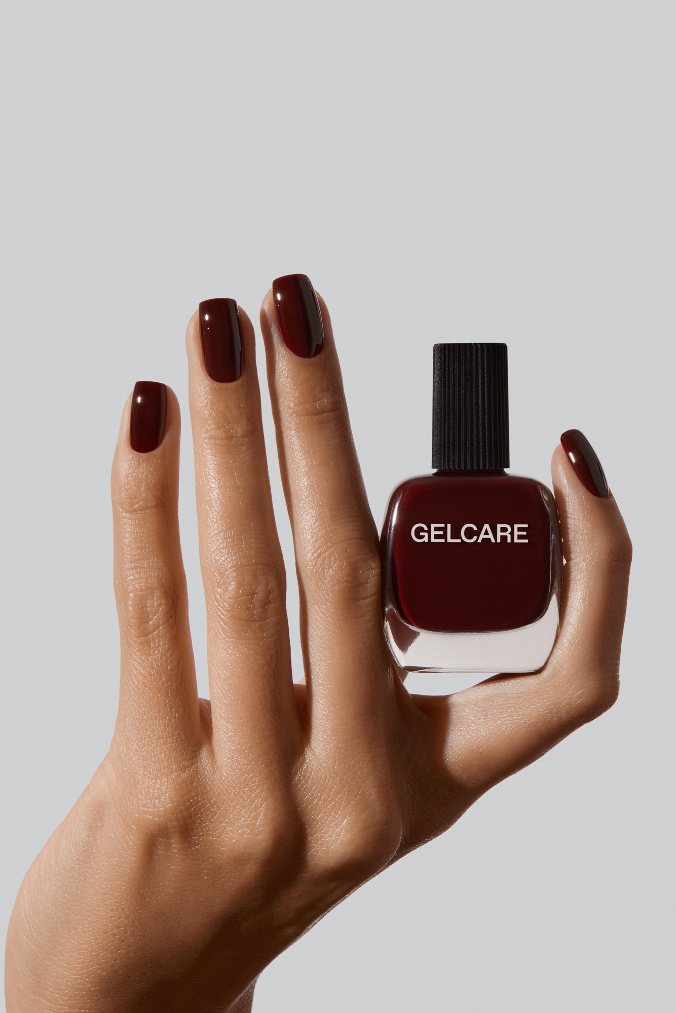 Bouteille de vernis rouge bourgogne Gelcare dans une main